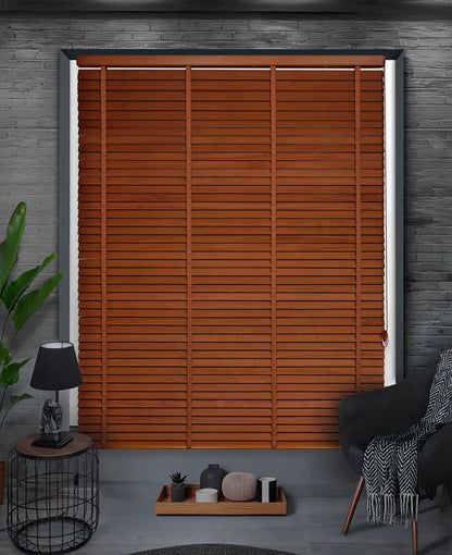 Wooden blinds in a room with a lamp, plant, and chair.